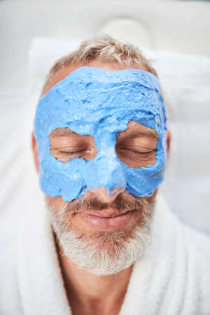 Close-up photo of an elderly gentleman face covered with a blue creamの写真素材