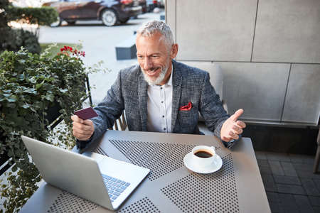 Professional-looking elder man gesturing actively while having a video-call and holding a plastic cardの写真素材