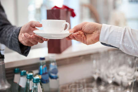 Cropped photo of waiter hand passing a cup of coffee to his customer at the barの写真素材
