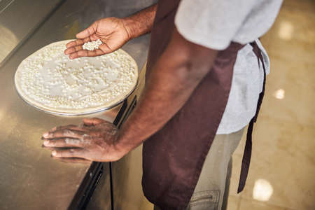 Top view cropped head close up of man in apron holding grated cheese while putting it on doughの写真素材