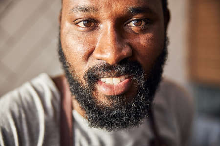 Close up cropped head portrait of joyful handsome stubbled Afro American chef in apron standing in pizzeria kitchenの写真素材