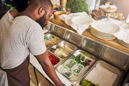 Top view of handsome bearded chef in apron standing near table with stuffing for making pizza