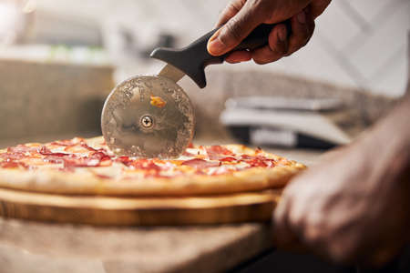 Close up of male hand slicing freshly baked pizza with round cutter wheelの写真素材
