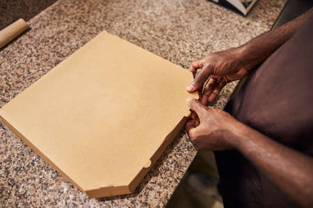 Close up of Afro American male hands packing freshly baked pizza in delivery boxの写真素材