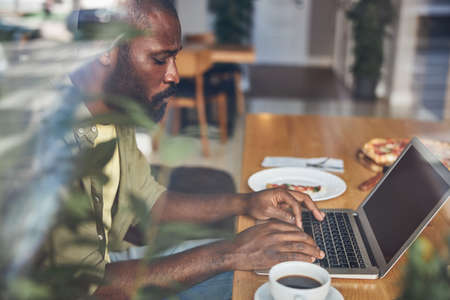 Serious bearded gentleman using modern notebook while sitting at the table in cafe