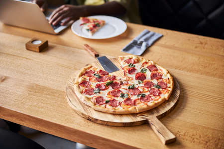 Close up male freelancer working on notebook while sitting at wooden desk with delicious pepperoni...