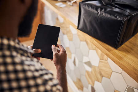 Close up of male hands holding electronic pad PC while man standing near counter with food delivery bagの写真素材