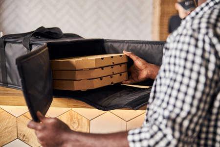 Close up of male courier hands placing cardboard pizza boxes in insulated thermal packing bag
