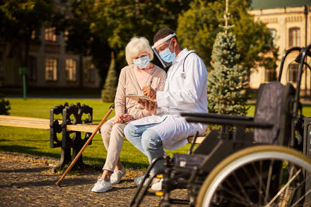 Full-length photo of a joyful medical practitioner writing in the notebook with a senior adult...