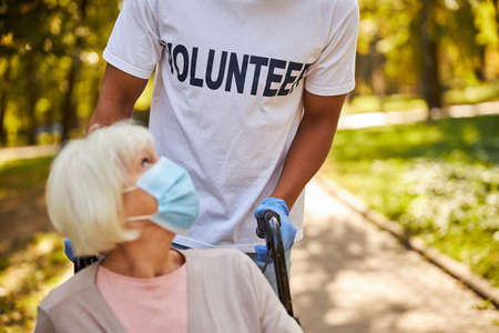 Cropped photo of an Afro-American volunteer wearing medical gloves and holding the handles of a wheelchair with an aging femaleの写真素材