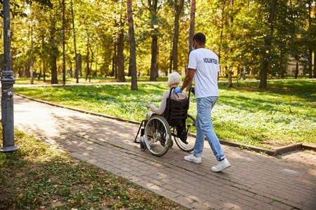 Full-length photo of supportive volunteer getting a retired old lady out of the parkの写真素材