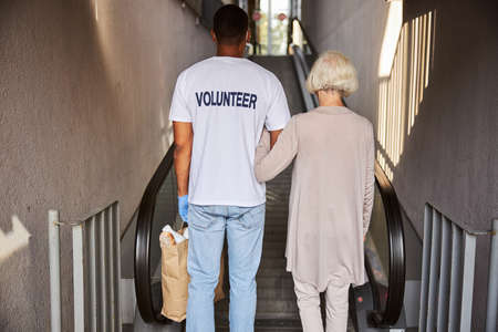 Caregiver and pensioner standing in front of an escalator with their backs to camera
