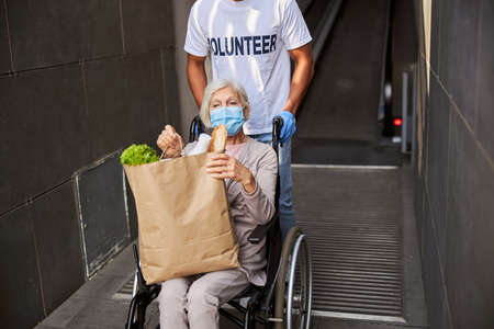 Disabled pensioner moving out of a department store using a wheelchair with the help of a caring...