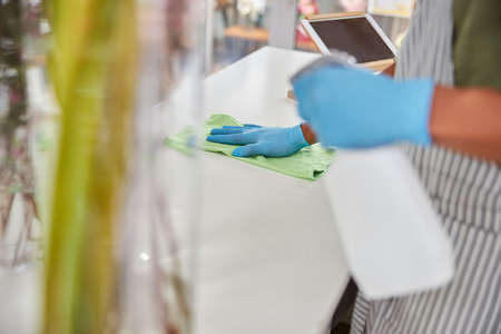 Top view cropped head close up of man in latex gloves doing desinfection in flower shop during...
