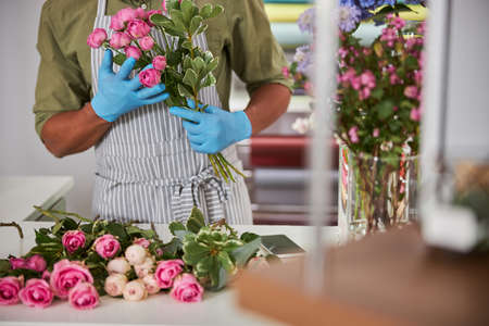 Cropped head of male florist in apron and latex gloves holding pink roses during working processの写真素材