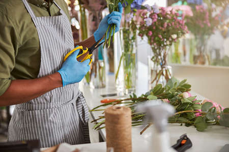 Cropped head of male in apron and latex gloves making bouquet during working day in shopの写真素材
