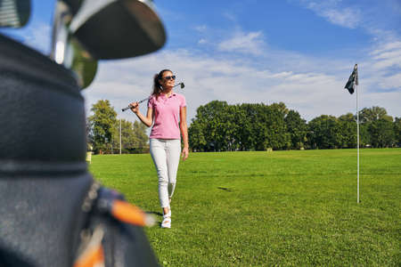 Full-length portrait of a smiling young fit female in sunglasses walking across the driving rangeの写真素材