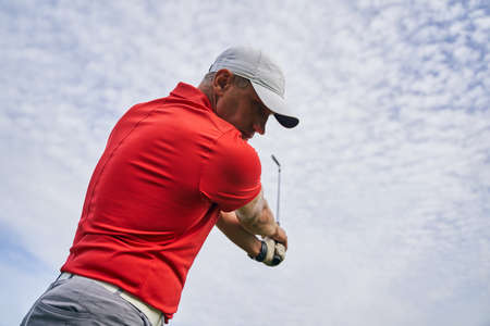 Serious concentrated golfer in a cap and a polo shirt holding a club in the air
