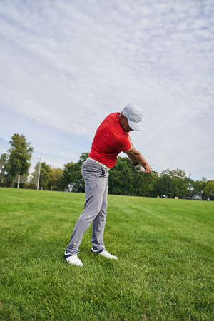 Skilled diligent adult male player with a club in his hands practicing his swing strokesの写真素材