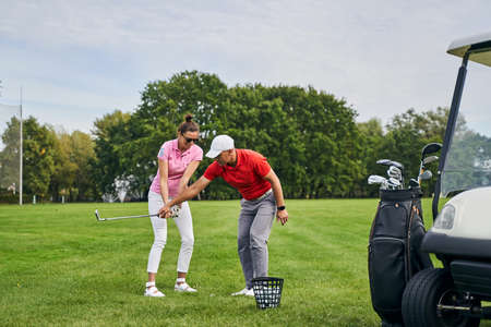 Cheerful female beginner learning to hit the ball with a mid-iron assisted by her trainerの写真素材