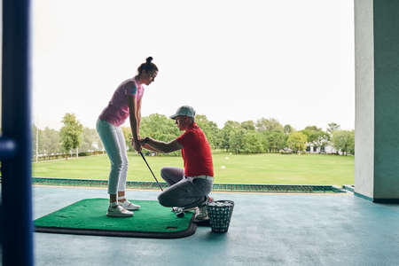 Side view of a golfer learning to grip the iron club helped by her coachの写真素材