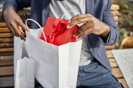 Focused photo on young man that putting present in bag and waiting for his girlfriend
