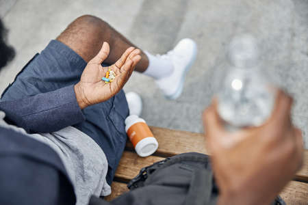 Young international man sitting on the bench looking at his palm, going to take medicineの写真素材