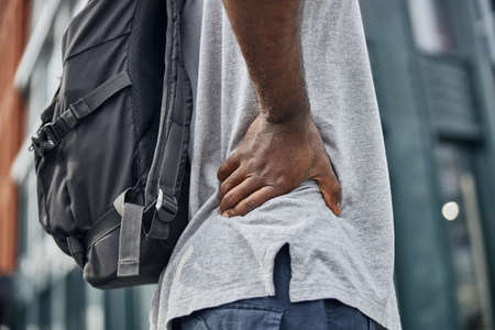 Active dark-skinned man putting hand on the back while having stop during walk