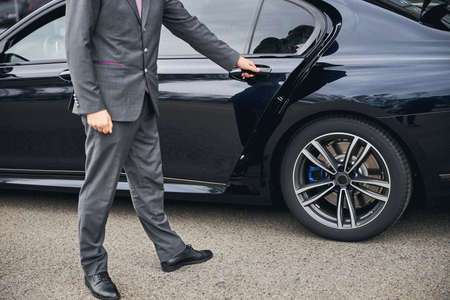 Cropped photo of a driver in a stylish suit opening the car door for his passengerの写真素材