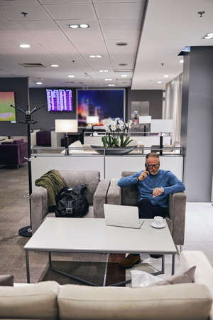 Serious male entrepreneur with a smartphone in his hand checking the time on his watch