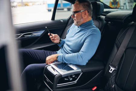 Attractive focused Caucasian male passenger in eyeglasses sitting in the back seat of the taxicab