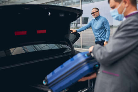 Pleased bearded middle-aged Caucasian man in eyeglasses leaning one hand on the open car door