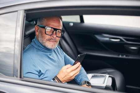 Serene attractive male passenger with a smartphone sitting in the car with an open window