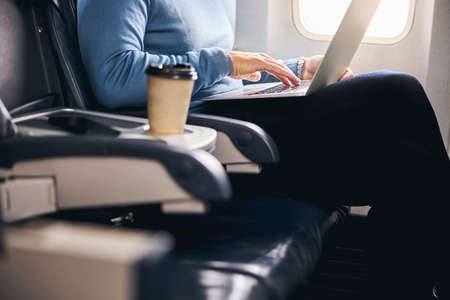 Cropped photo of a Caucasian man in casual clothes working on his computer during the flight