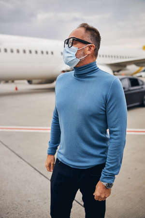 Male tourist in a face mask standing at the airdrome in front of the aircraftの写真素材