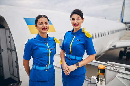 Front view of two beautiful Caucasian flight attendants in airline uniforms smiling at the camera
