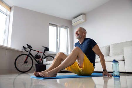 Man laying his legs on a sport carpet while supporting himself with arms behind his back