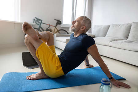 Peaceful man putting one leg over another while keeping his hands on a floor behind himの写真素材