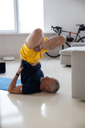 Athlete in yellow shorts lifting his legs and back in the air while lying on his neck on the floor