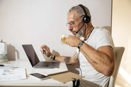 Businessman bringing a glass to his lips and cooling his drink while carrying out his task at a...