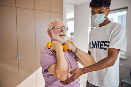 Elderly man working out with dumbbells assisted by a professional instructor in a face maskの写真素材