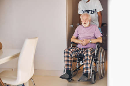 Front view of a pensive disabled person being transported by a caregiver to the kitchenの写真素材