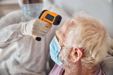 African American healthcare professional in a hazmat suit using an infrared thermometer for the forehead temperature measurementの写真素材