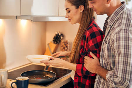 Side view of an attractive lady holding a bowl of egg mixture over the skilletの写真素材