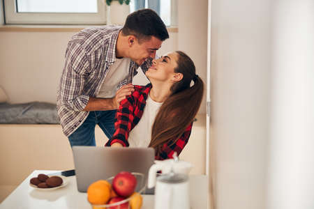 Affectionate young handsome husband bending towards his smiling attractive female spouse with a long...