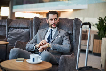 Serious entrepreneur in an armchair setting the watch on his left hand to the right timeの写真素材