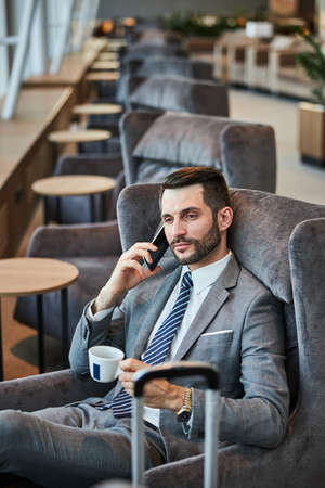 Pleased male enjoying his coffee while discussing important business matters on the mobile phone in...