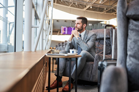 Businessman resting the chin on his hands while giving a long pensive look into an airport windowの写真素材