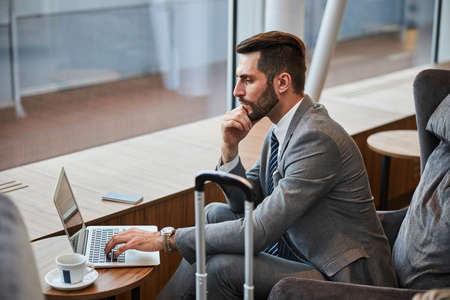 Business owner looking at laptop display and typing on a keyboard while doing his work remotely from an airportの写真素材