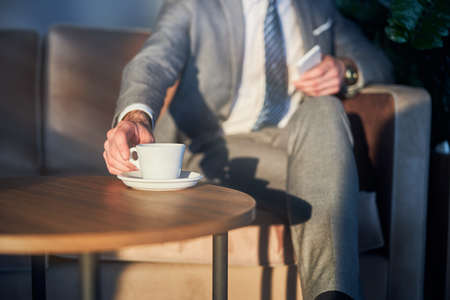 Cropped photo of a man reaching out and picking his drink from a coffee table
